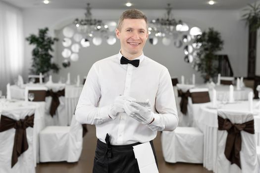 Waiter in a white shirt and bow tie writing down an order in a cafe