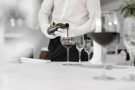 Male waiter in white gloves pours red wine into a glass