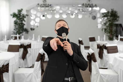 Showman in a suit and protective mask with a microphone in his hands in the banquet hall of rastoran