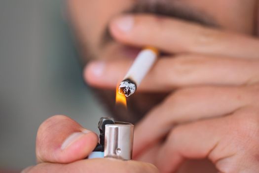 Closeup of young man lighting and smoking cigarette. Smoking addiction and bad habit concept