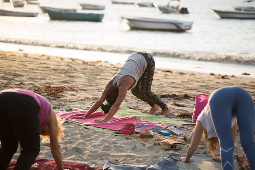 Women doing yoga exercises or supported pigeon pose on an empty beach of the Indian ocean in Mauritius.