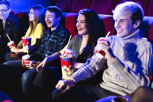 Friends sit and eat popcorn together while watching movies in a movie theater.