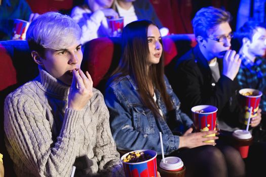 Young man eats popcorn in the cinema and watches a movie