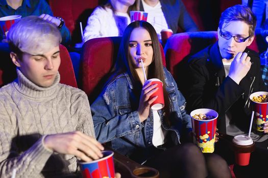 Cheerful company in the cinema. A girl drinks from a glass, a man eats popcorn