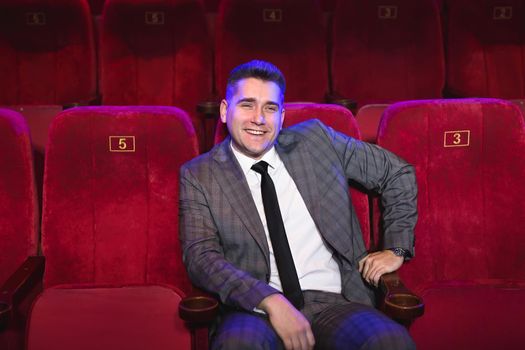 Portrait of a young handsome man alone in a movie theater in a business suit.