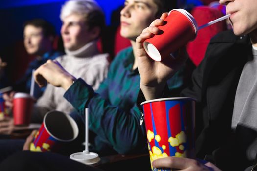 Glasses with a tube and popcorn in the hands of people in a movie theater close-up