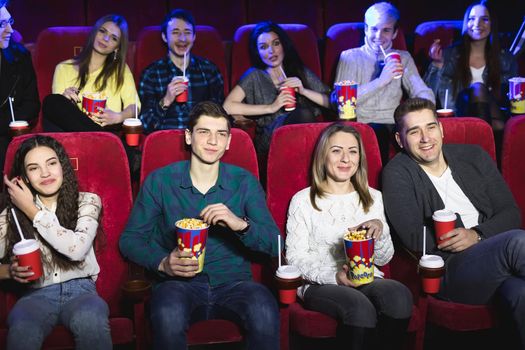 Friends sit in a cinema watch film eating popcorn and drinking aerated sweet water. Movies and entertainment concept.