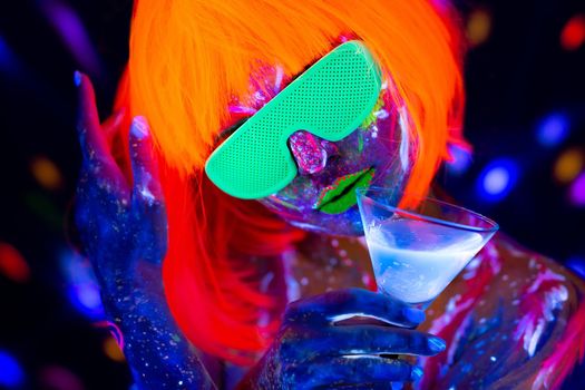 Fashion model woman drinking alcoholic cocktail in neon light, disco night club. Beautiful dancer model girl colorful bright fluorescent make-up.