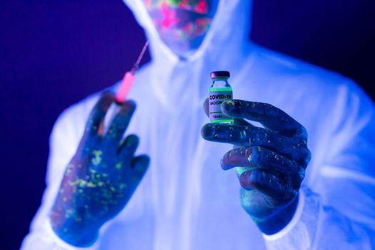 Doctor in ultraviolet neon light is holding COVID-19, oronavirus vaccine and syringe using for prevent infection. Medicine and Healthcare concept.