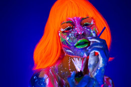 Woman with a cigarette in neon light. Beautiful model girl colorful bright fluorescent makeup. Dangers of smoking.