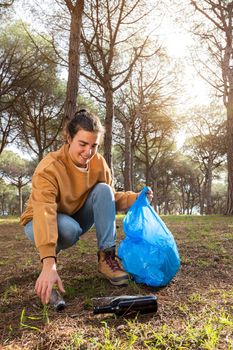 Happy young caucasian woman picking up plastic bottle cleaning forest. Copy space. Vertical image.