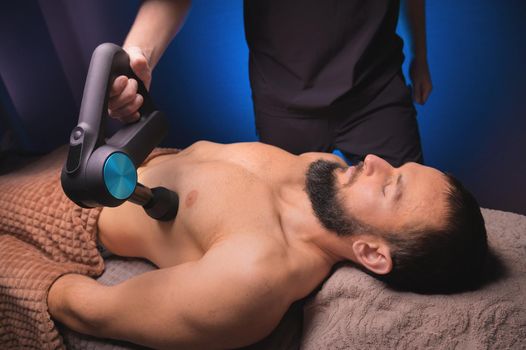 Close-up of a Caucasian male pectoral muscle percussion massager working out in a professional massage parlor