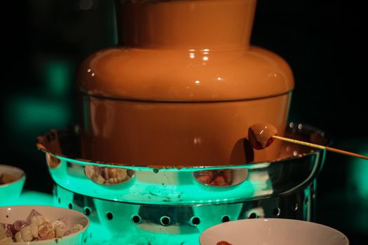 Strawberry skewer being dipped into a chocolate fountain fondue, at a wedding in Hampshire, UK.