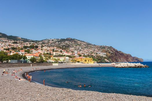 Sunbathers on the pebble beach coast of Funchal, Madeira, Portugal.