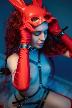 naked girl in a red rabbit mask and long red gloves poses sexually in leather belts and a collar for bdsm games