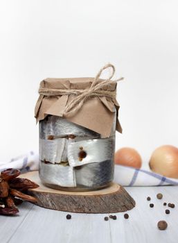 Pickled herring, pepper and spices in a jar on the table, light background, vertical photo