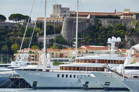 Monaco, Monte-Carlo, a lot of large motor yachts are parked side by side in the port, with huge fenders between them to avoid collision at sunny day, mooring ropes go into the azure water