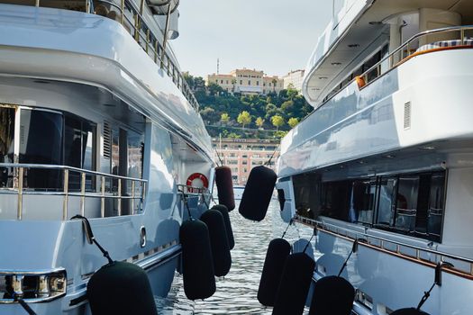 Monaco, Monte-Carlo, two large motor yachts are parked side by side in the port, with huge fenders between them to avoid collision at sunny day, mooring ropes go into the azure water
