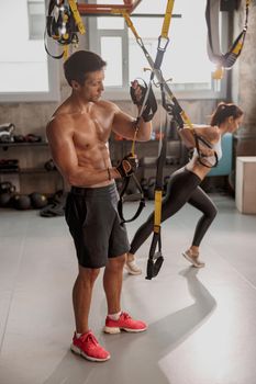 Strong man and beautiful slim woman doing exercises at gym