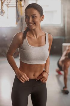 Beautiful female with perfect slim body wearing workout wear looking away and smiling while posing in sports club
