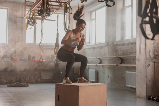 Shot of female athlete jumping on wood box during sport training in fitness center