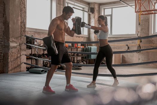 Slim woman wearing boxing gloves working on blow with coach