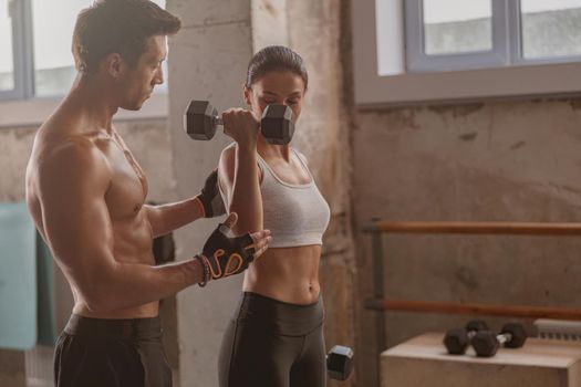 Muscular man in the gym with athletic woman performing sports exercises