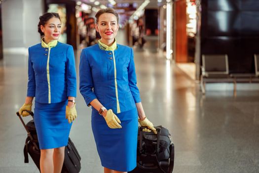 Two smiling women stewardesses in air hostess uniform walking down airport terminal