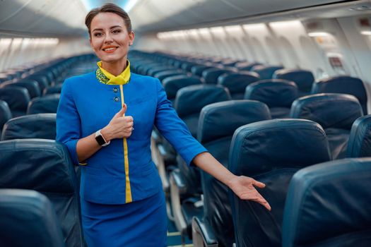 Smiling stewardess pointing at passenger seat in airplane cabin