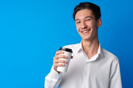 Teenager boy drinking a cup of coffee over blue background