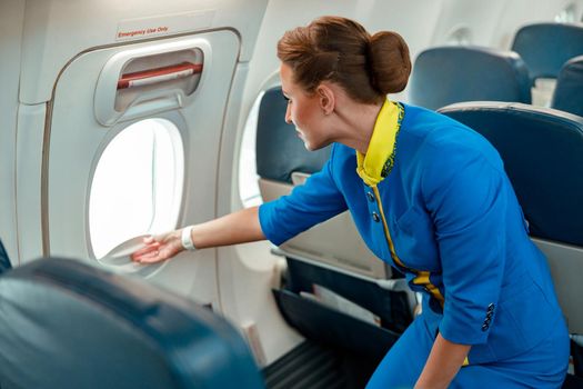 Female flight attendant opening window in airplane