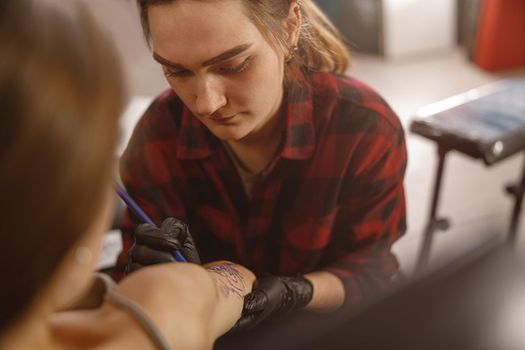 Young tattoo artist drawing on the client skin