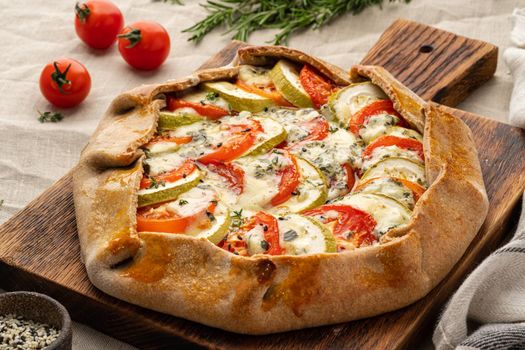 Homemade savory galette with vegetables, wholegrain pie with tomatoes, zucchini, side view