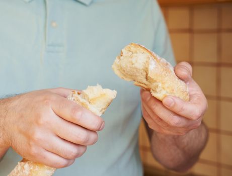 Man breaks off hunk of fresh baked homemade crusty bread baguette. Delicious