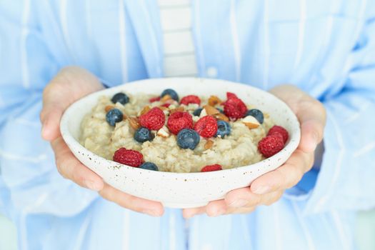 Faceless woman holds in hands breakfast, oatmeal porridge with berries and nuts