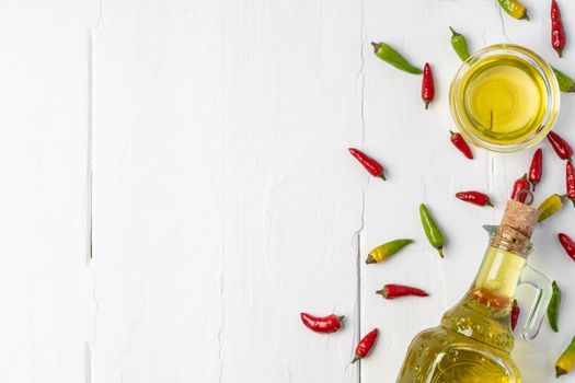 Chili peppers and olive oil bottle on white wooden background, top view