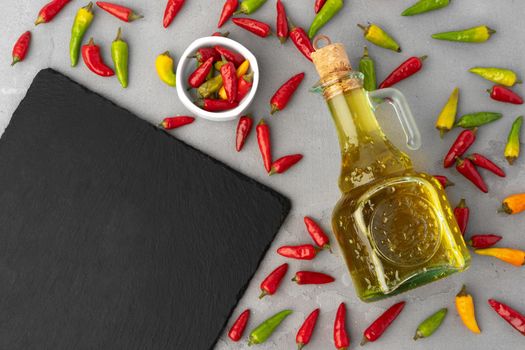 Olive oil, chili peppers and stone cutting board on gray background