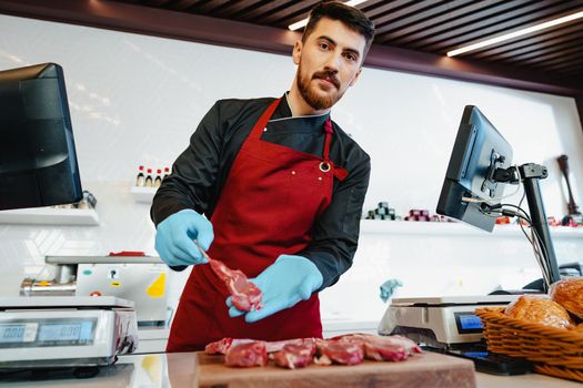 Young butcher holding raw lamb ribs in a butcher shop
