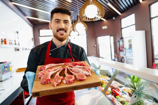 Young butcher holding raw lamb ribs in a butcher shop