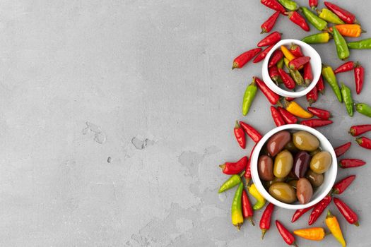 Chili peppers and marinated olives on gray background