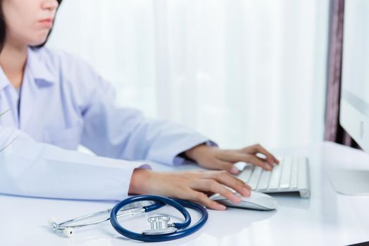 Female doctor with stethoscope typing on keyboard desktop computer