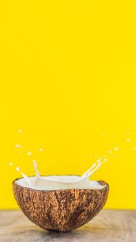 Coconut fruit and milk splash inside it on yellow background VERTICAL FORMAT for Instagram mobile story or stories size. Mobile wallpaper