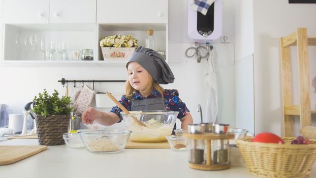 Cute little girl chef pointed hand on bowls with ingredients for cooking