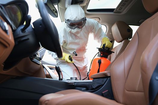 Worker cleanse car interior with spray disinfectant in container