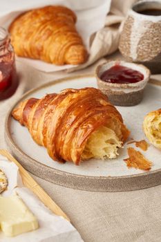 Two delicious croissants on plate and hot drink in mug. Morning French breakfast with fresh pastries and jam. Light gray background, side view, vertical