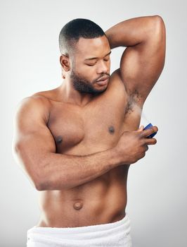 Keeping sweat at bay. Studio shot of a handsome young man spraying deodorant on his armpit against a white background.