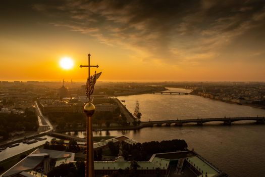 The golden angel on the cross of the Peter and Paul Fortress at sunrise, reflection of the orange sky on the water, drawbridges Troitsky and Liteiny