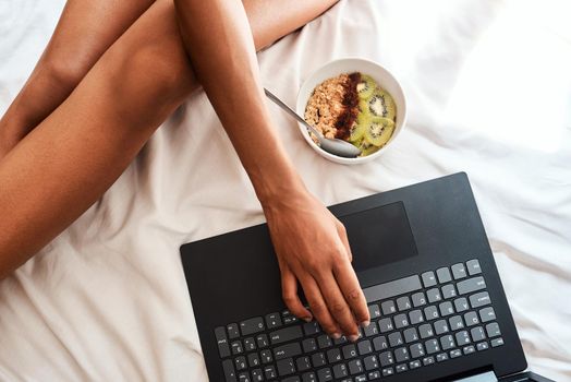 I got this breakfast idea online. Cropped shot of an unrecognizable woman sitting on her bed with her laptop and a bowl of oats.