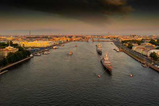 Aerial landscape with warships in the Neva River before the holiday of the Russian Navy at early morning, warships pass under a raised drawbridge, the latest cruisers among landmarks, Palace bridge
