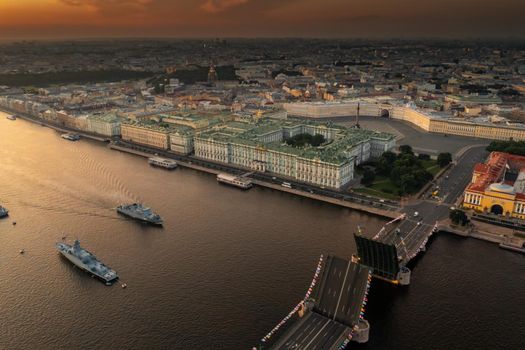 Aerial landscape with warships in the Neva River before the holiday of the Russian Navy at early morning, warships pass under a raised drawbridge, the latest cruisers among landmarks, Palace bridge